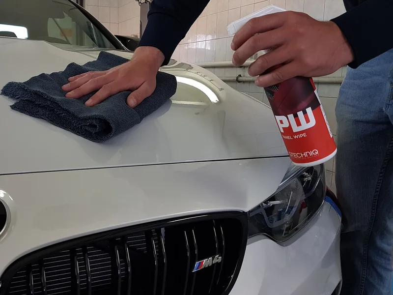 Ruční otření kapoty bílého BMW mikrovláknem před ošetřením laku